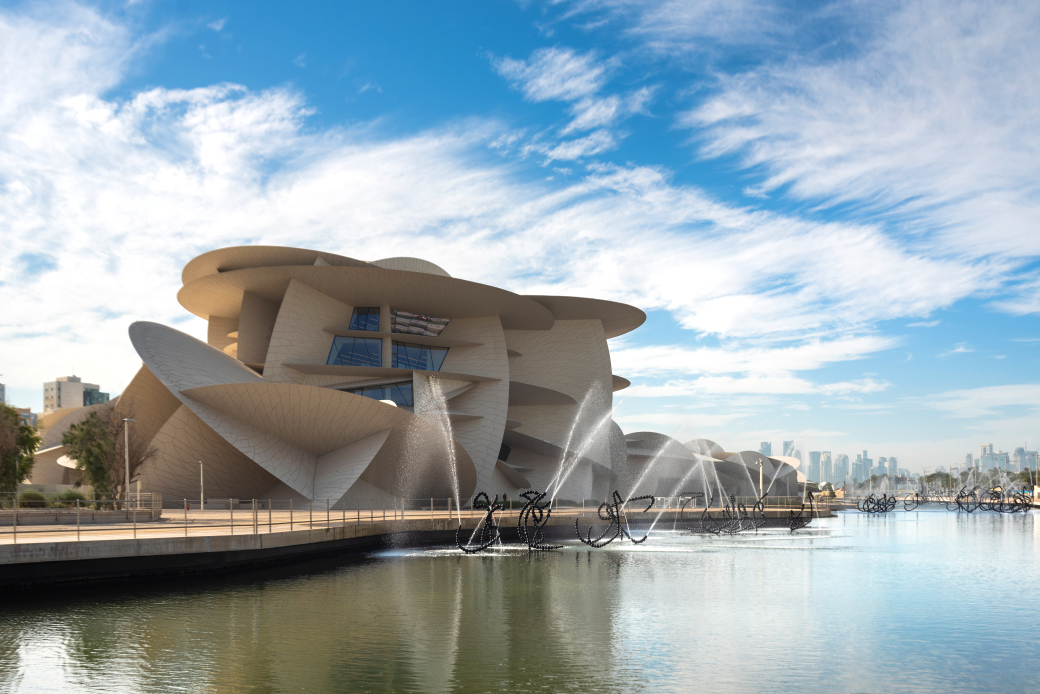 ジャン・ヌーヴェル設計のカタール国立博物館。砂漠の結晶「デザートローズ」を思わせる建築の向こうに、ドーハの近代的なスカイラインが広がる。matpit73 - stock.adobe.com