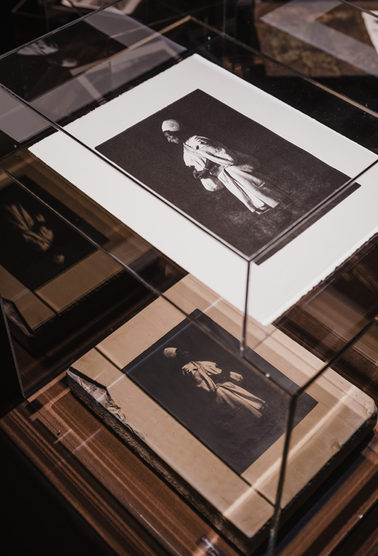 石板を使って印刷されたリトグラフ作品。アクリルボックスの下にあるのが石板、上に刷り上がった作品が展示されている。「高木由利子 写真展　Threads of Beauty 1995-2025」展示風景、Bunkamura ザ・ミュージアム、2026年　Photo by Ooki JINGU