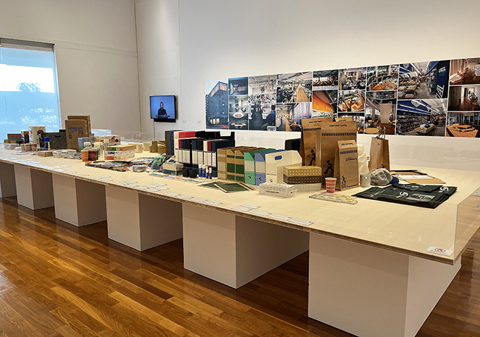 世田谷美術館で開催中の「宮城壮太郎展――使えるもの、美しいもの」会場展示より。壁面には、宮城はデザインディレクターを務め、2001年に開設された、アスクル本社「e-tailing center」の様子が写真パネルで展示されている。