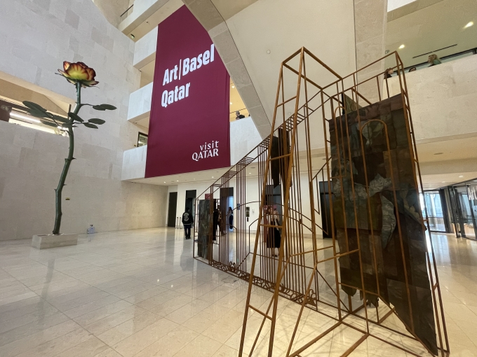 M7のアトリウム。常設されているドイツの現代アーティスト、イザ・ゲンツケンの巨大な一輪のバラをモチーフにした彫刻作品《 ローズ III 》のそばに展示されたリビア出身のヌール・ジャウダのインスタレーション《 二つの家の間にある家》。アート・バーゼル・カタールの特別プロジェクト作品のひとつ。