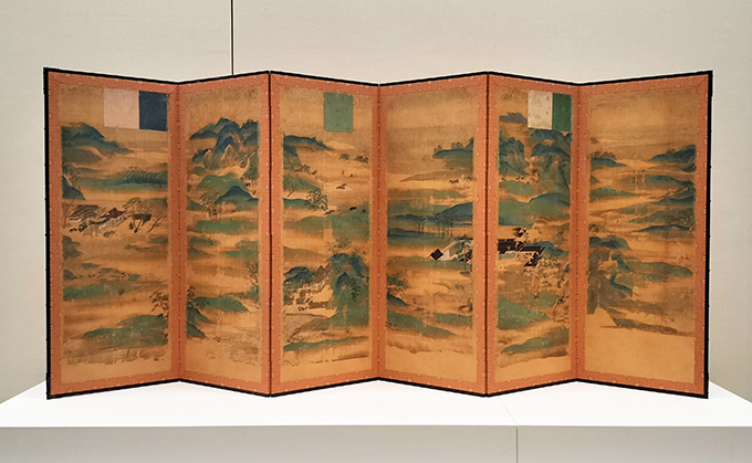 （会場風景より）国宝《山水屛風》6曲1隻 鎌倉時代・13世紀 京都・神護寺【展示期間：10/11～11/5】
現存最古の「やまと絵屛風」の作例。なだらかに山々が連なる中で日本の貴族たちの姿が見える。